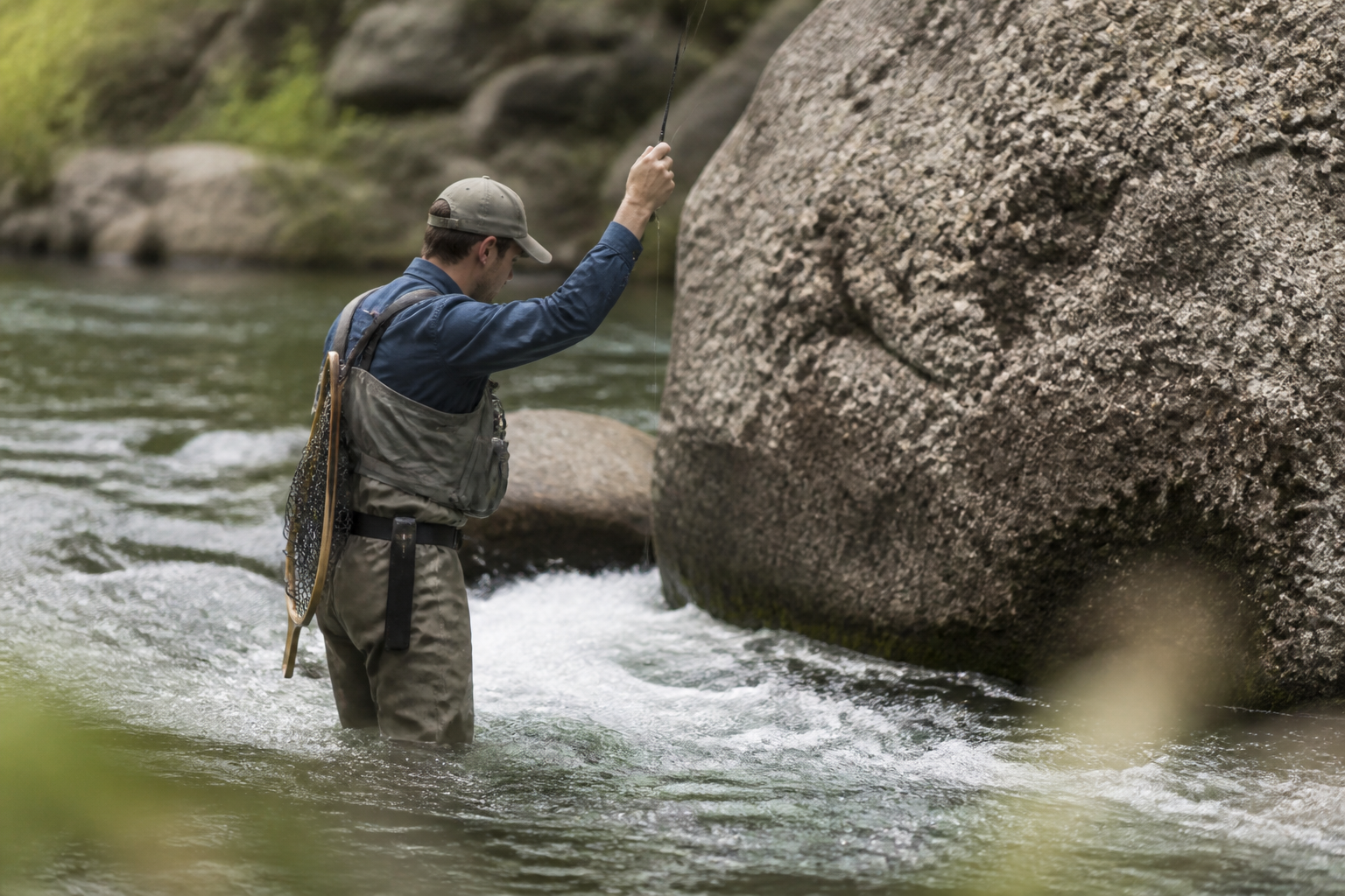 A fly angler standing close to a boulder holding the rod high while short line nymphing a narrow seam of fast pocket water